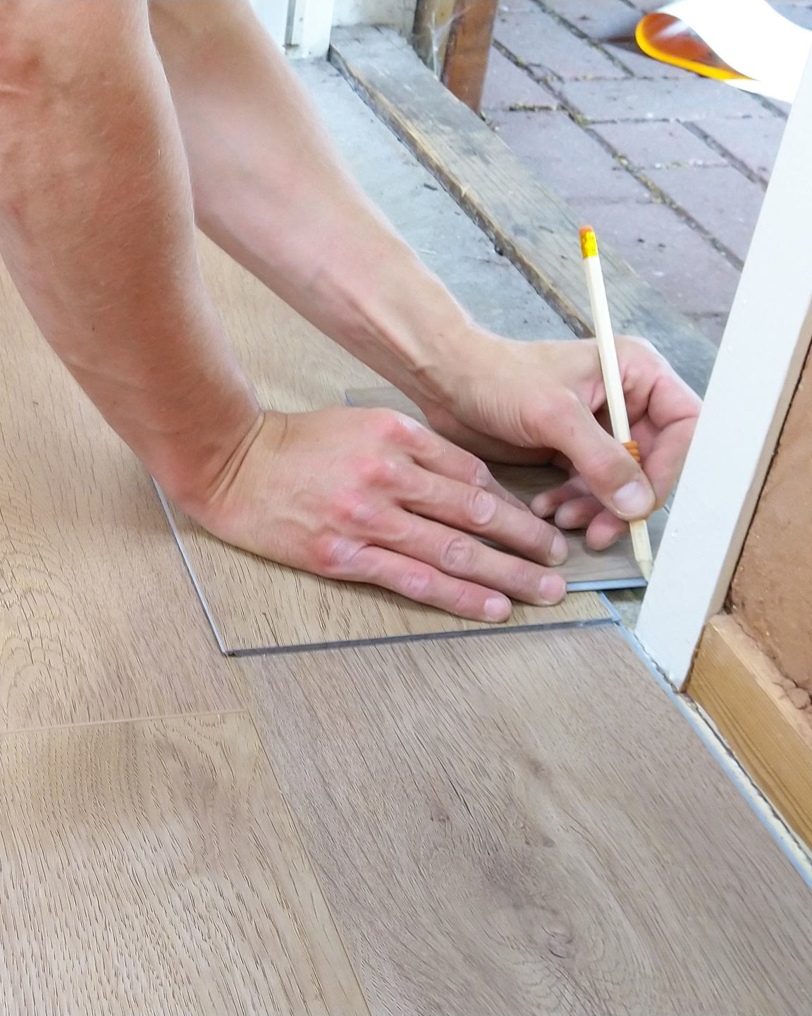Hands marking a laminate floor plank with a pencil