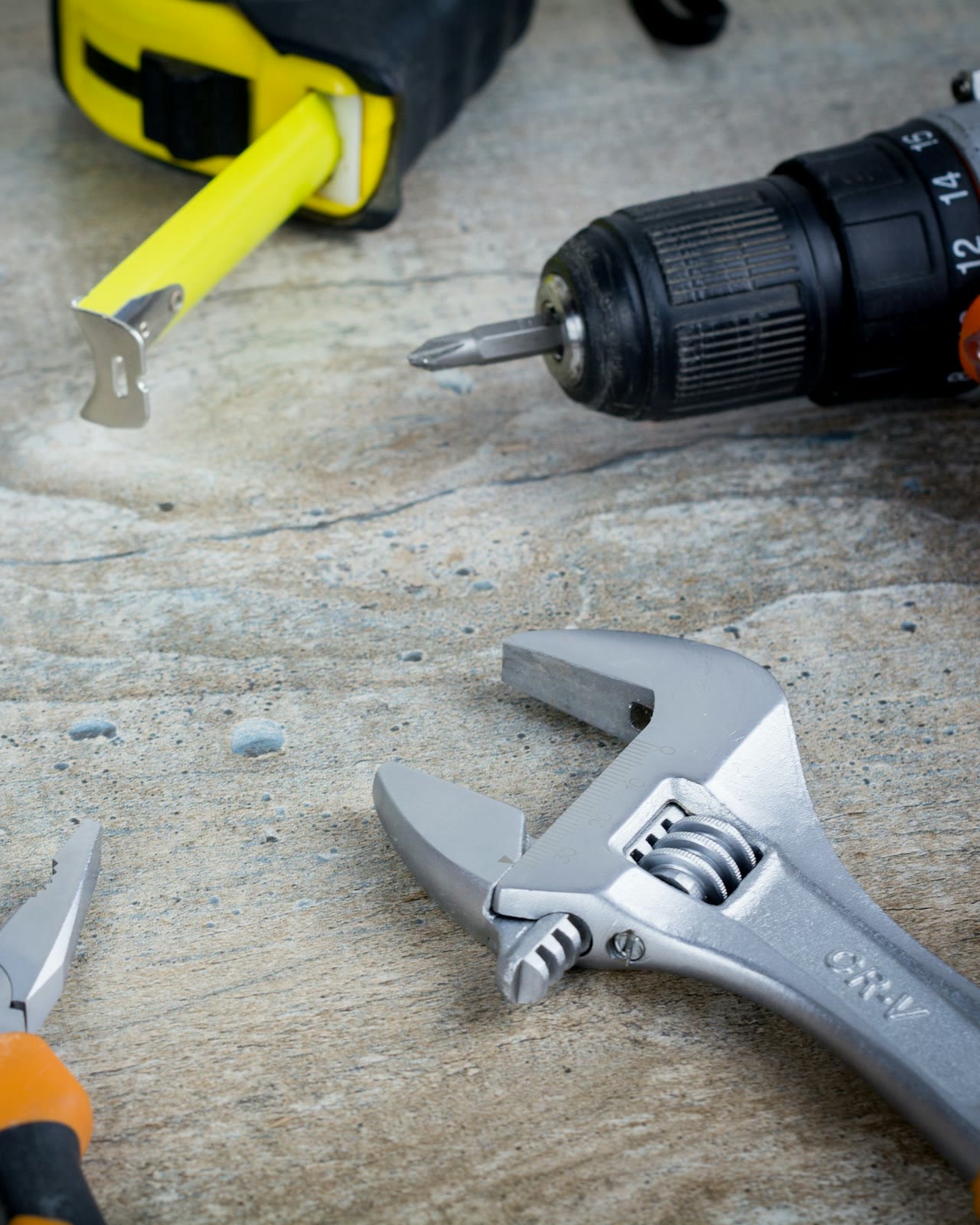 Pliers, an adjustable wrench, a tape measure and a drill on a workbench