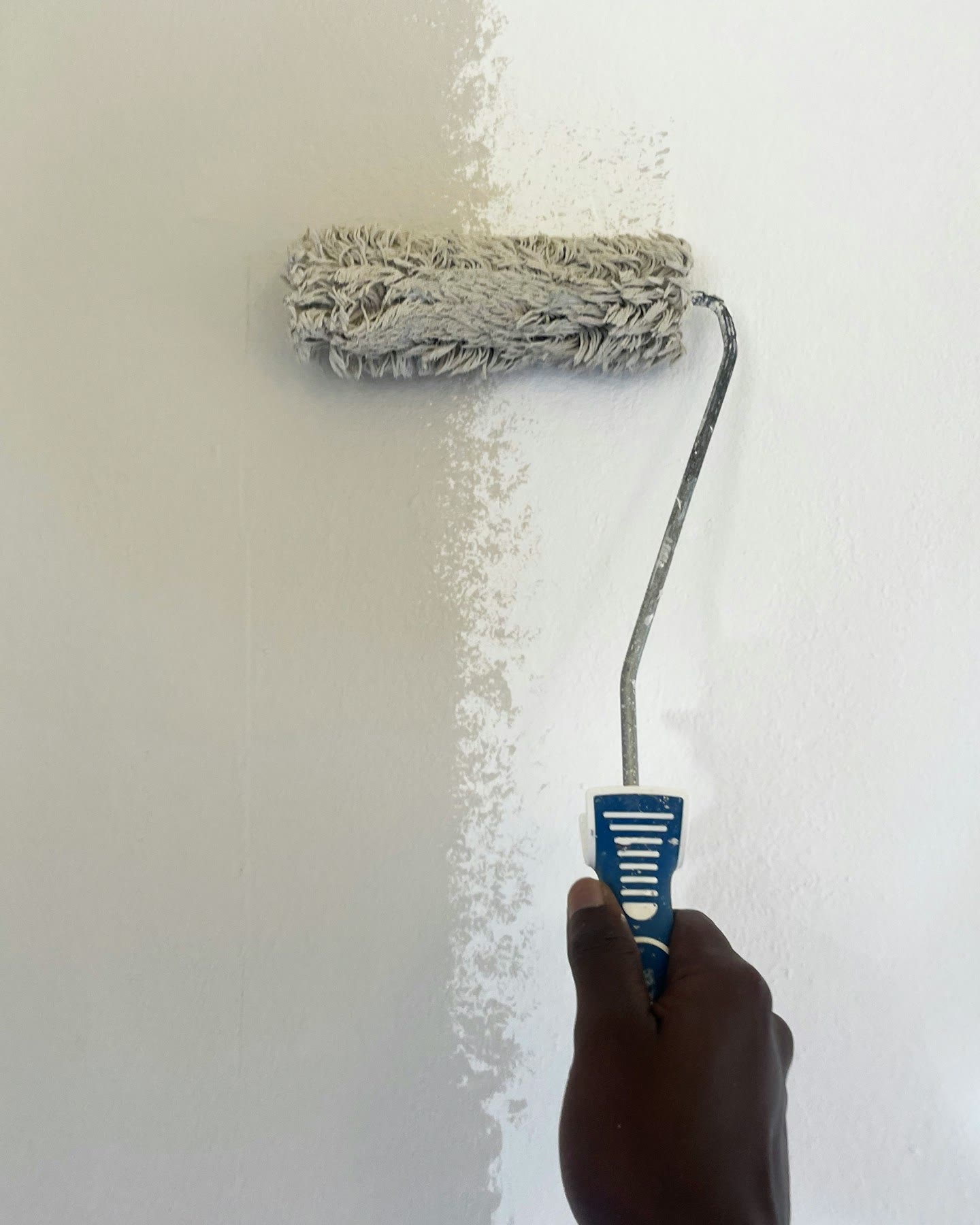 A paint roller putting a fresh coat of white paint on a wall